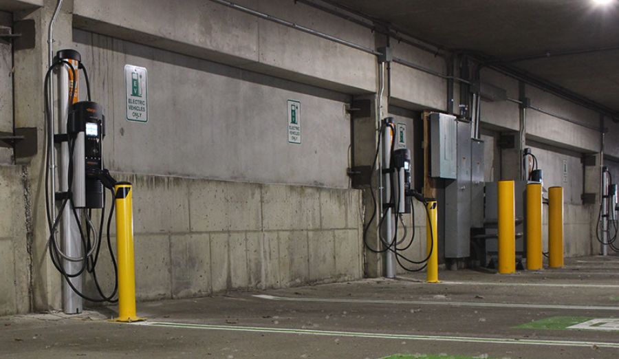 Parkkihallin seinustalla useita sähköautojen latauspisteitä, joissa on keltainen suojatolppa.